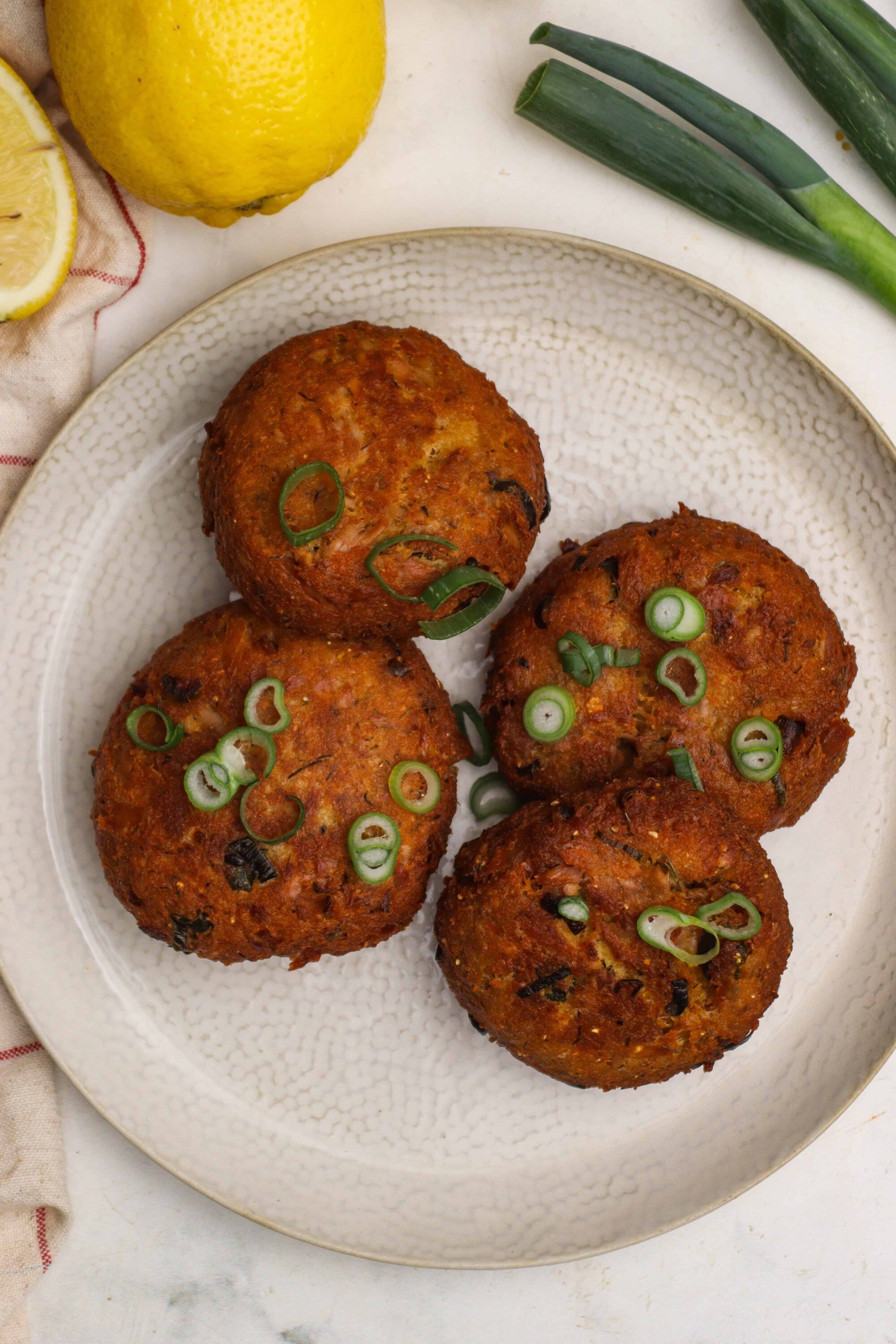 Crispy vegetable fritters garnished with green onions, served on a textured white plate.