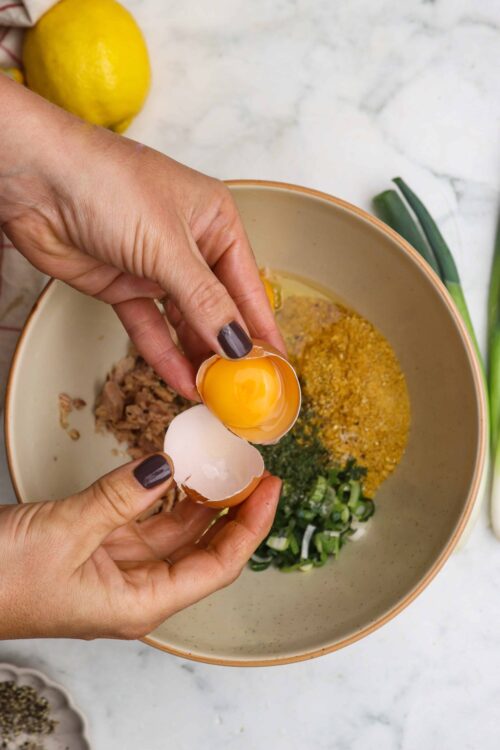 Cracked egg being added to bowl with chopped green onions and spices for baking or cooking recipe.