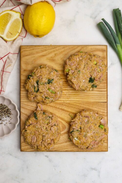 Savory chicken and leek patties on a wooden cutting board with lemons and green onions in the background.