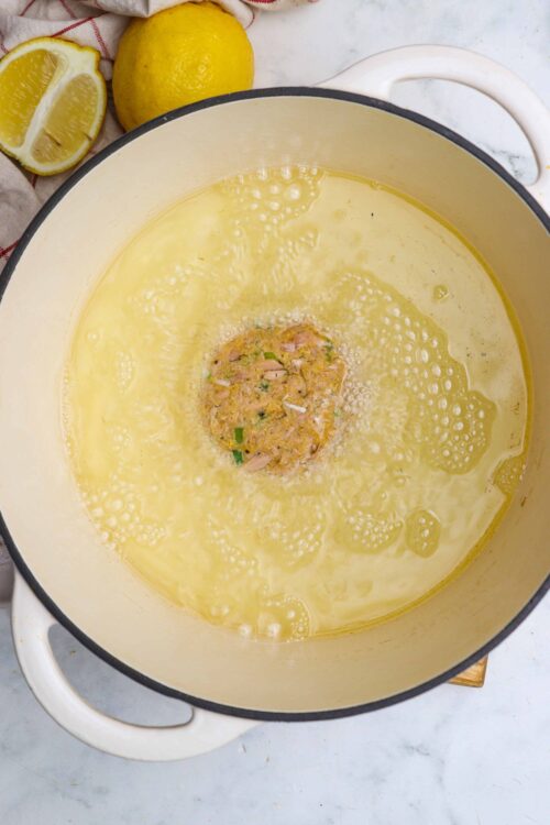 Juicy lemon chicken meatball mixture in a pot with lemon slices and fresh lemons nearby.