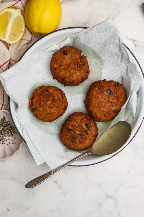 Golden fried crab cakes with herbs on a white platter.