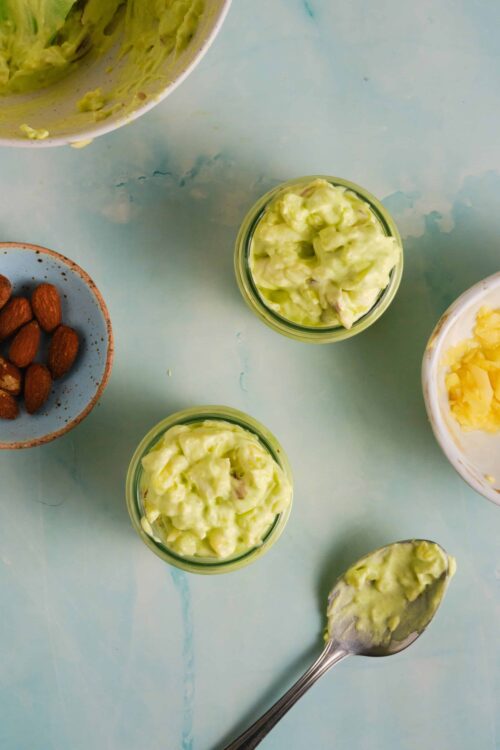 Creamy avocado mashed with lime and seasoning on a light blue surface.