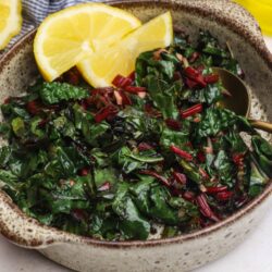 Fresh sautéed kale salad with lemon wedges and balsamic vinegar.