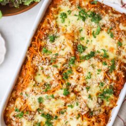 Baked spaghetti with cheese and fresh parsley in a white baking dish.