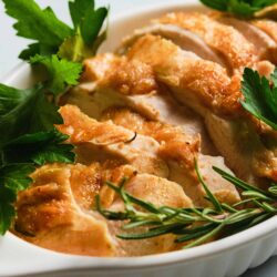 Buttered roasted chicken with fresh herbs in a white baking dish, crispy skin, and aromatic rosemary garnish.