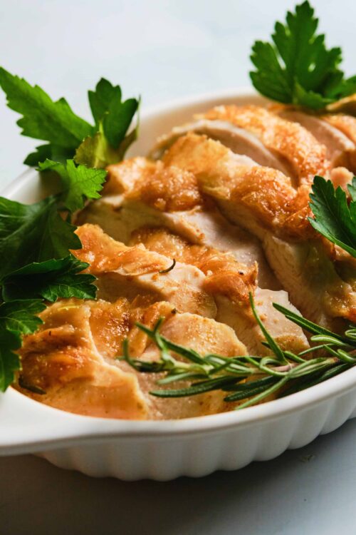 Buttered roasted chicken with fresh herbs in a white baking dish, crispy skin, and aromatic rosemary garnish.