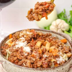 Savory beef bolognese served over pasta with grated Parmesan cheese in a rustic bowl.