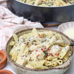 Creamy pasta with cheese, spinach, and cherry tomatoes in a rustic bowl.