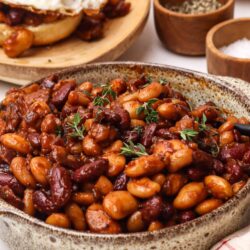 Savory baked beans with herbs in a rustic bowl for hearty comfort food.