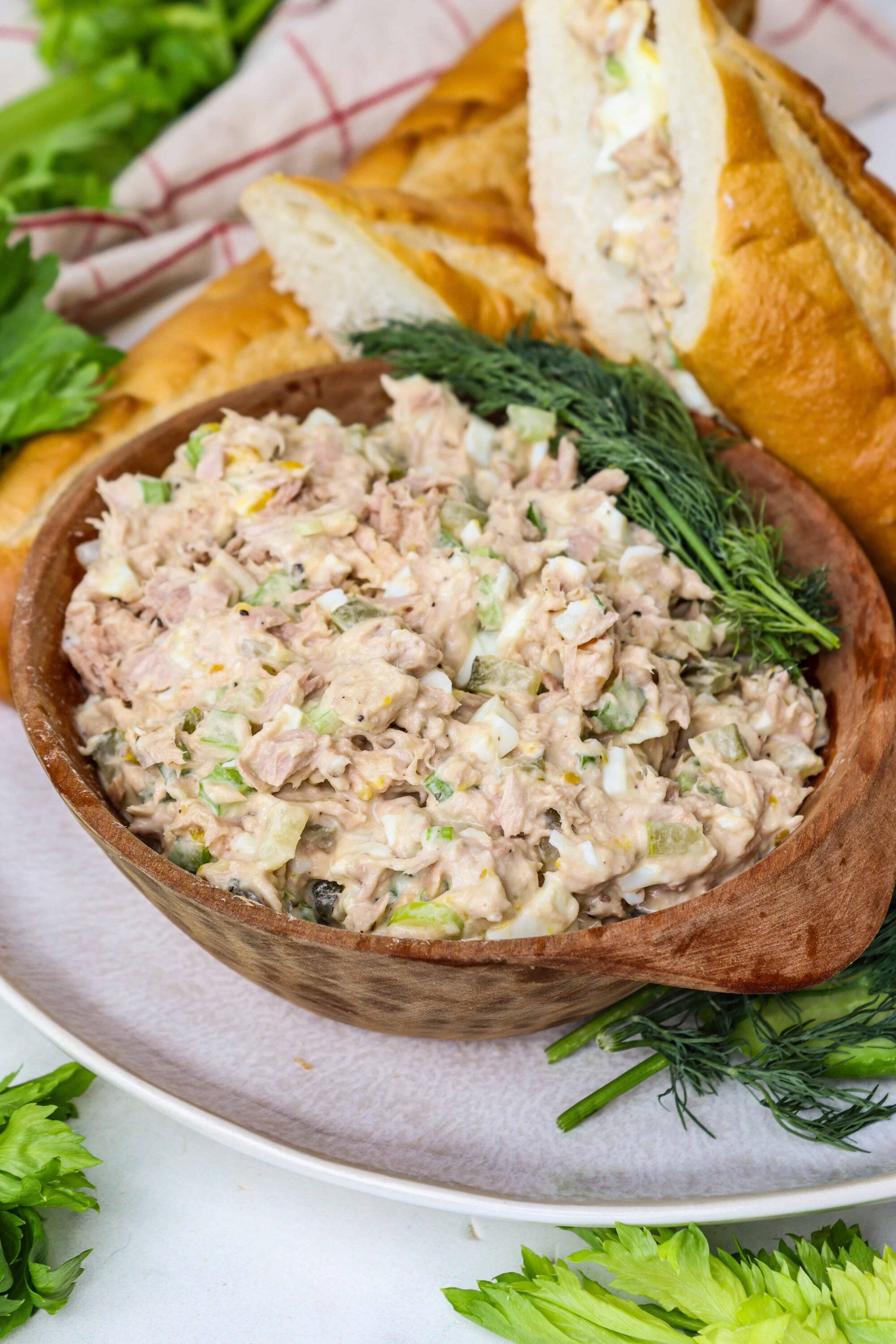 Creamy chicken salad in a wooden bowl with fresh herbs, served with sandwich bread and greens.