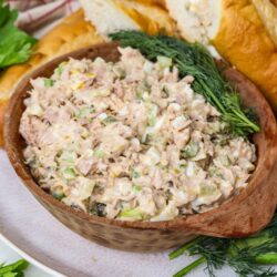 Creamy chicken salad in a wooden bowl with fresh herbs, served with sandwich bread and greens.