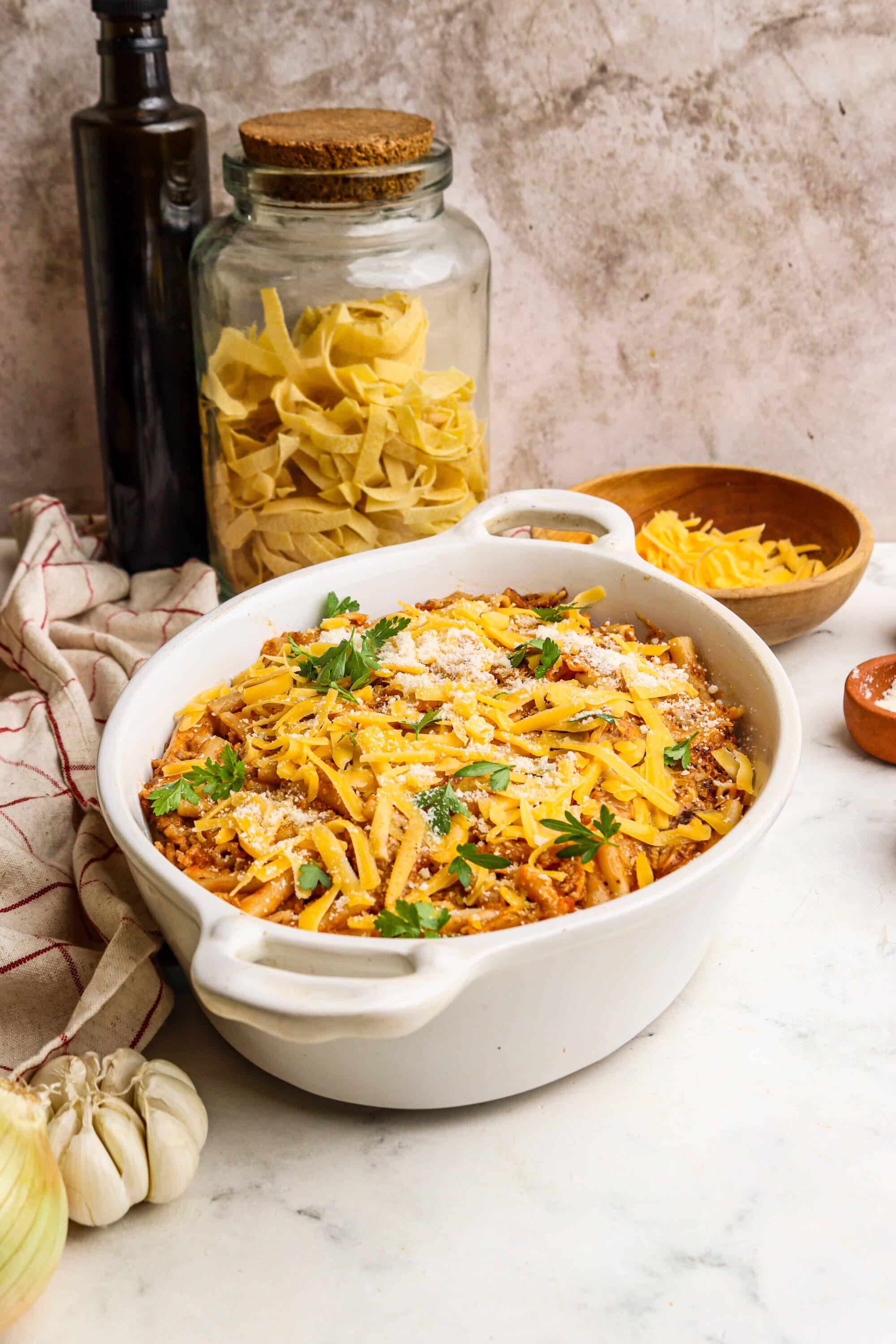 Creamy baked ziti pasta with cheese, ground beef, and fresh herbs in a white baking dish.