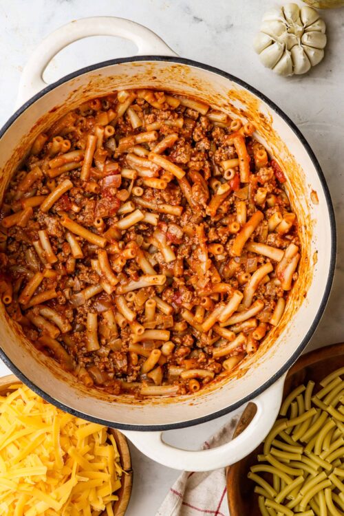 Savory baked pasta casserole with ground beef and tomato sauce, cheese, and pasta noodles in a white pot.