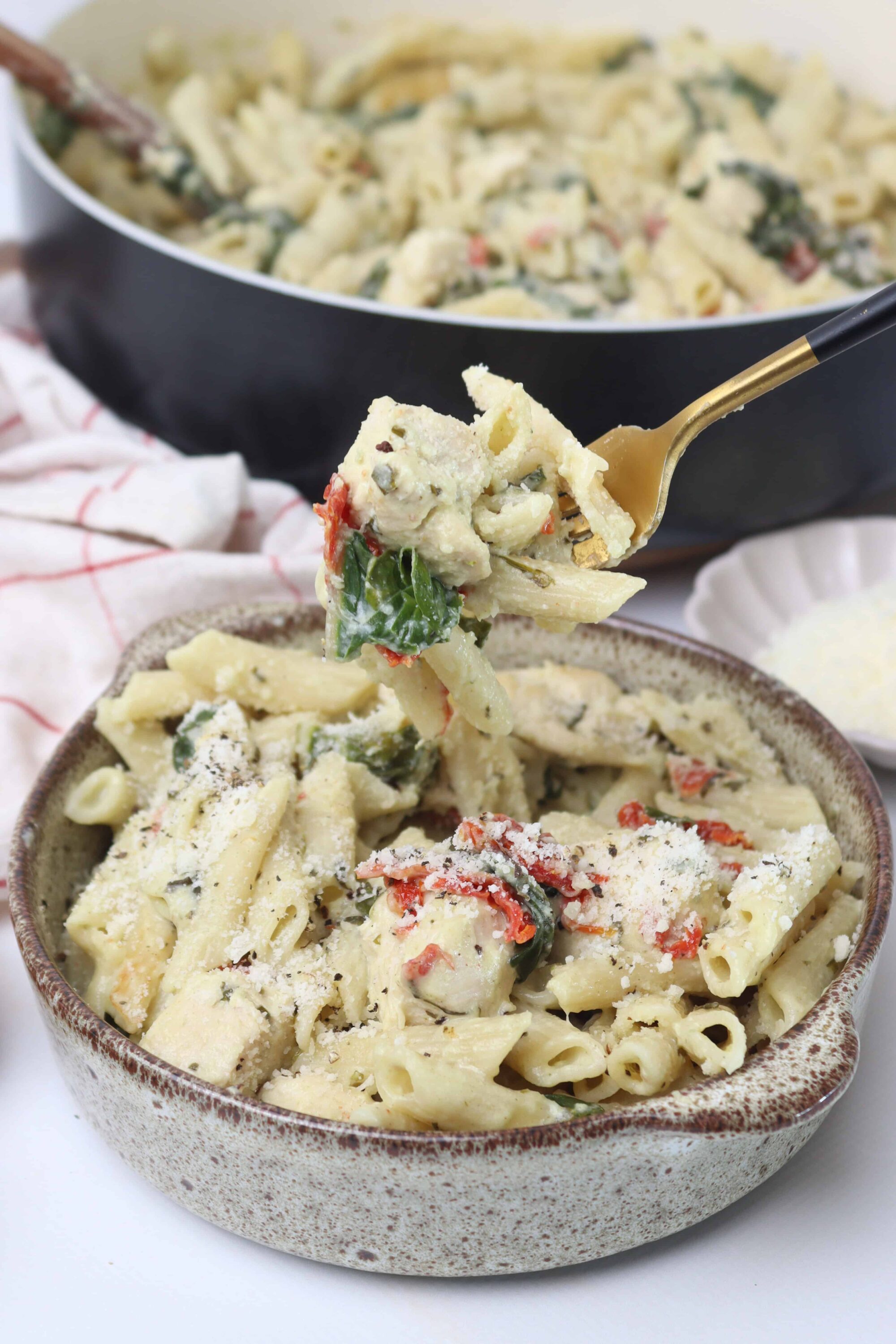 Creamy baked pasta with spinach, sun-dried tomatoes, and Parmesan cheese in a rustic bowl.
