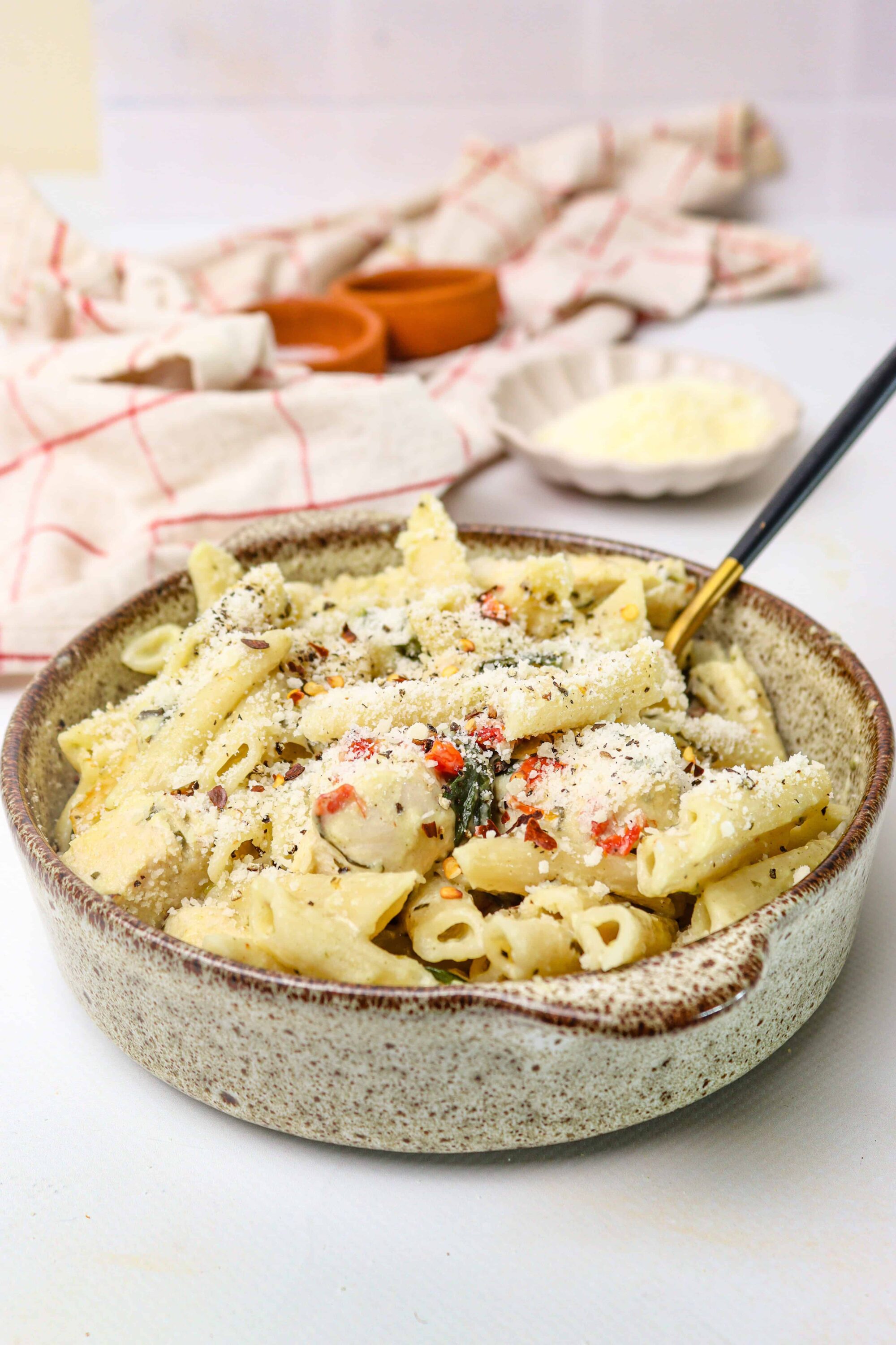Creamy chicken and cheese pasta baked in a rustic bowl, topped with parmesan and red pepper flakes.
