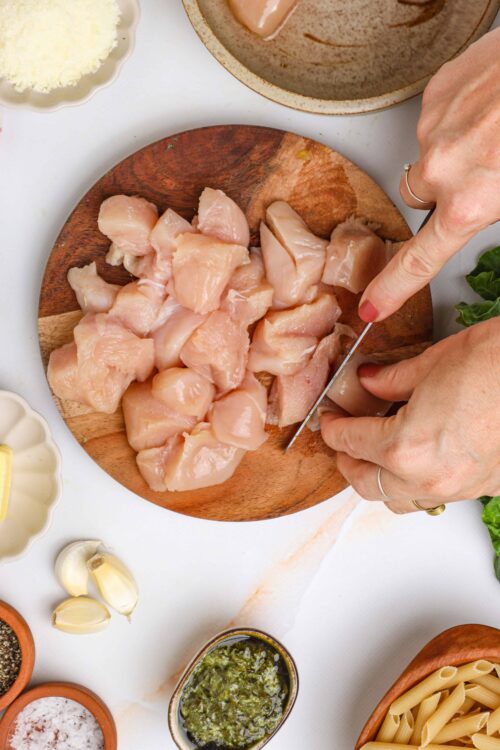 Diced raw chicken being cut on a wooden cutting board for a delicious Baked Bree recipe.