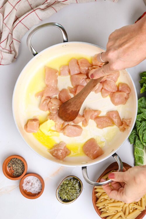 Juicy raw chicken pieces cooking in a creamy sauce for homemade chicken pasta dish.