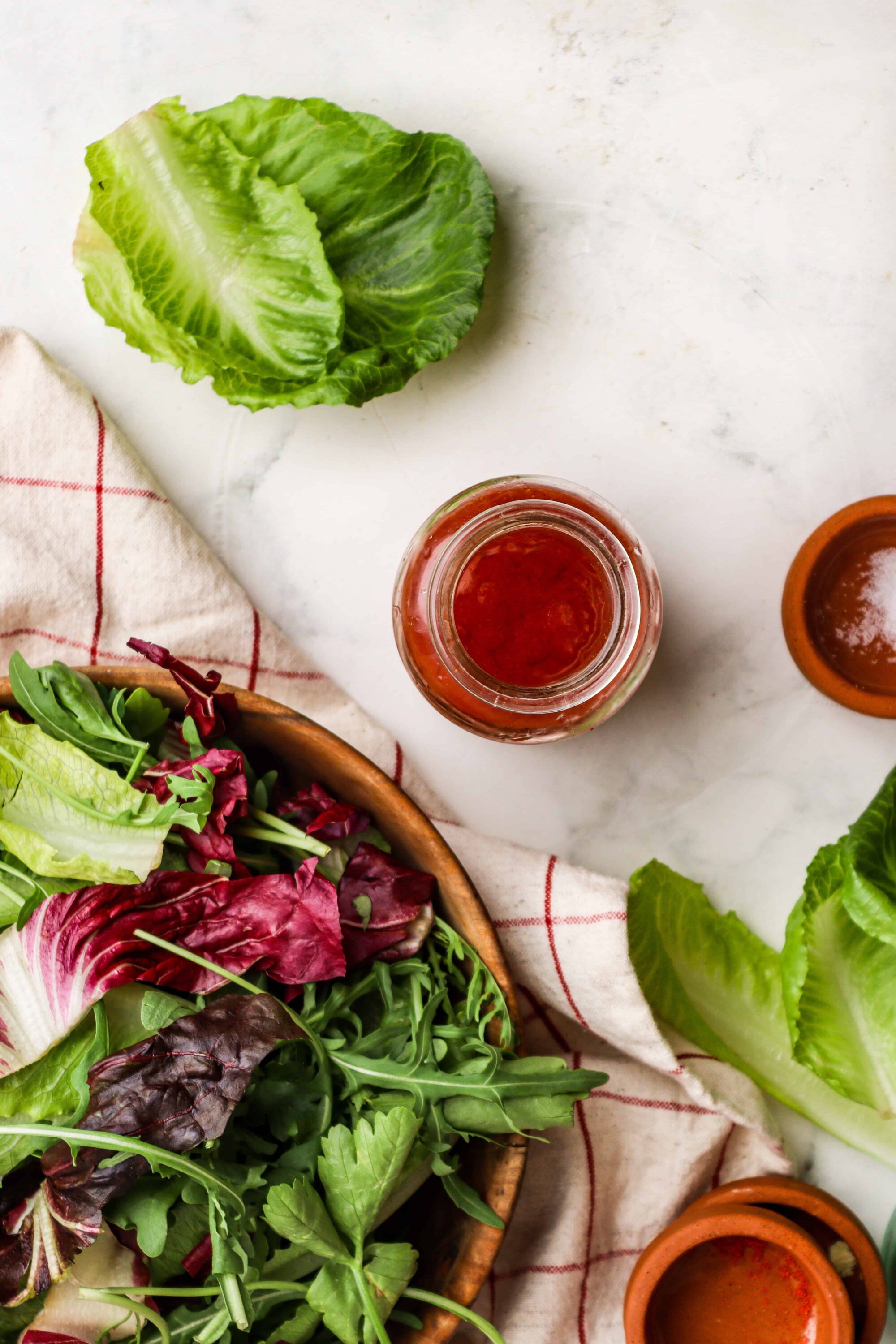 Fresh mixed greens and lettuce salad with vinaigrette and salad dressing jars on a white marble surface.