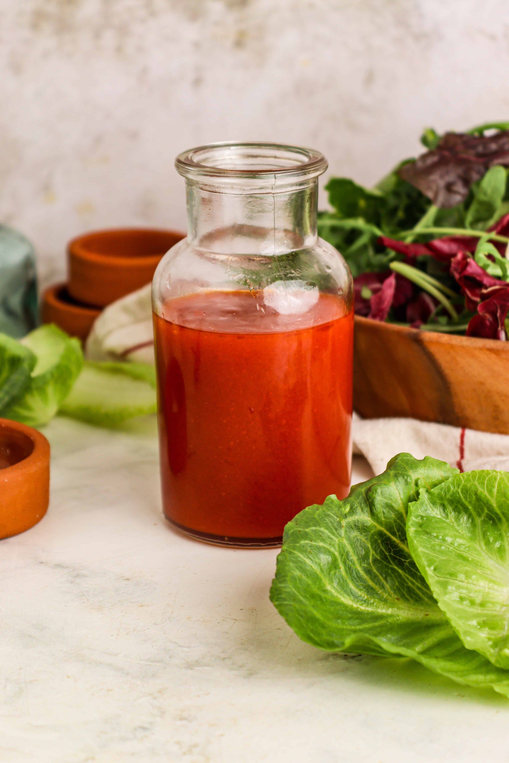 Vinegar in glass bottle with fresh salad ingredients on white surface.