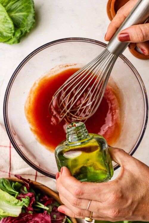Fresh vinaigrette being prepared with olive oil and red wine vinegar in a glass bowl.