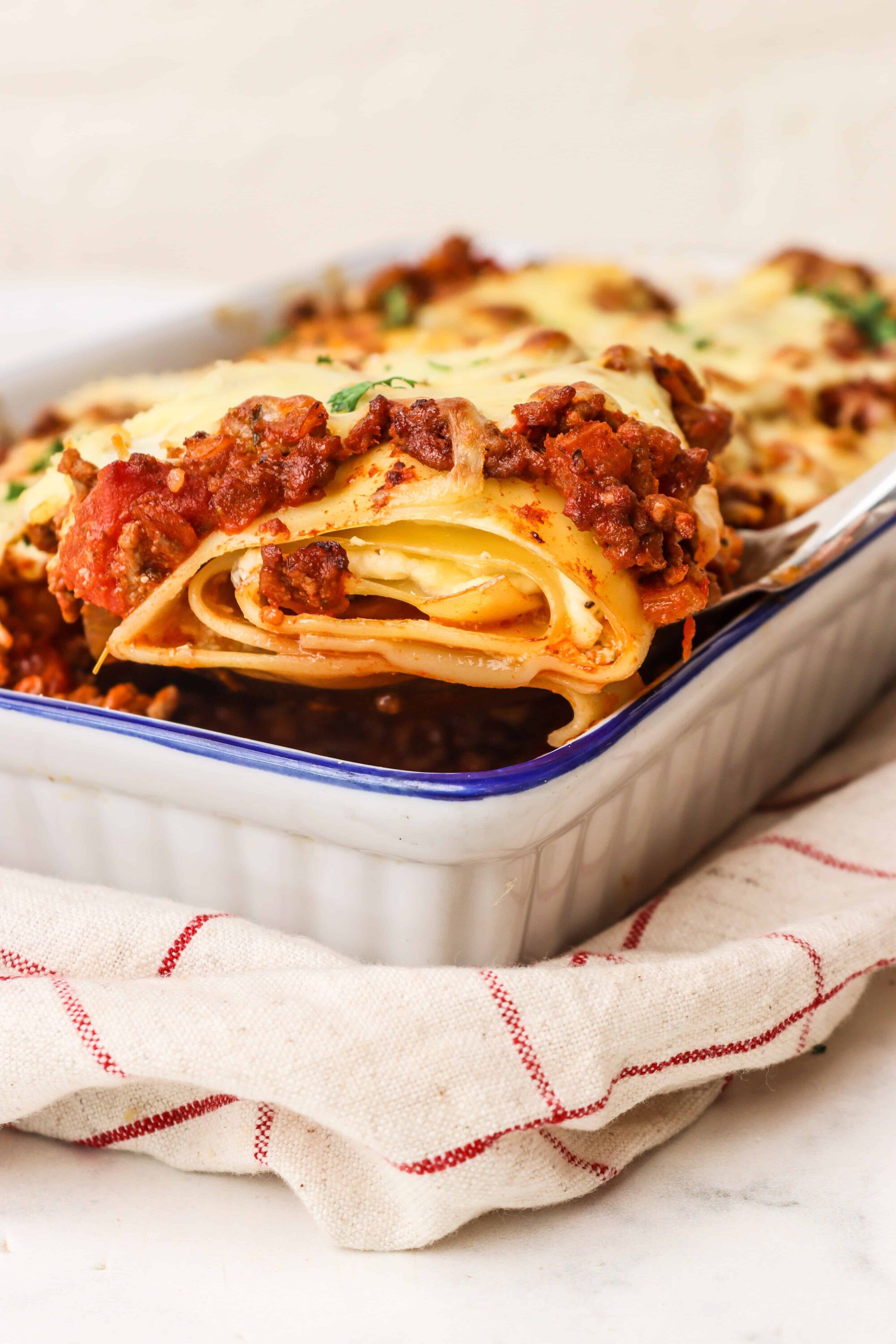 Savory lasagna baked in a white casserole dish topped with melted cheese and rich meat sauce.