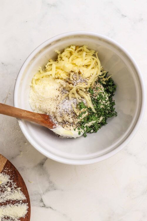 Shredded cheese, herbs, and seasonings in a mixing bowl for cheesy baking recipe.