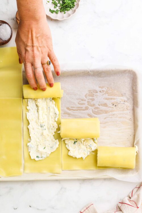 Buttered puff pastry with herb cream cheese filling on baking sheet, preparing for baking.