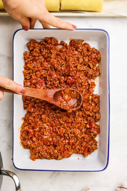 Savory homemade beef chili cooking in a white baking dish with a wooden spoon.