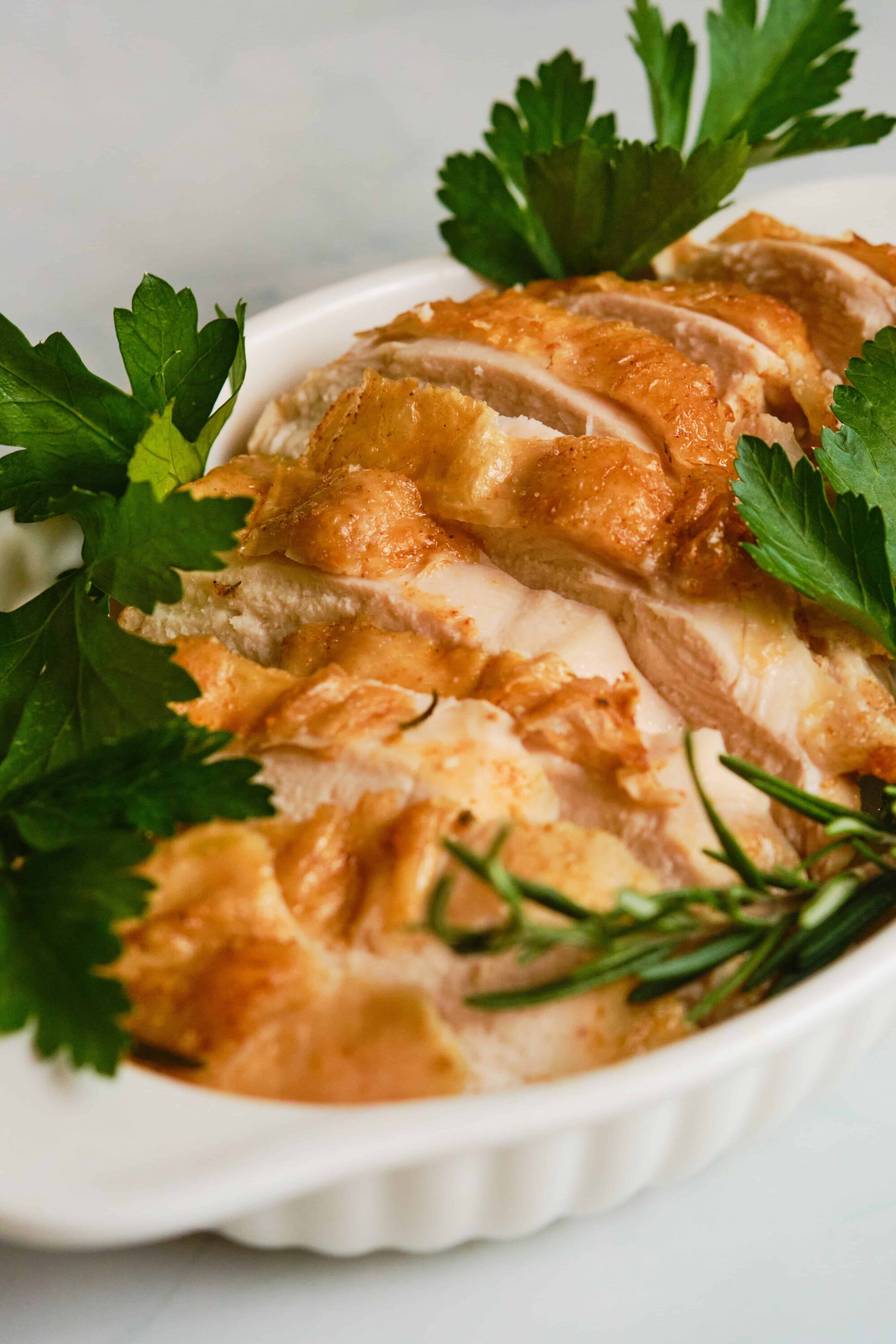 Juicy roasted chicken breast with fresh herbs and garnishes on white ceramic dish.