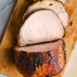 Juicy baked turkey breast sliced on a wooden cutting board.