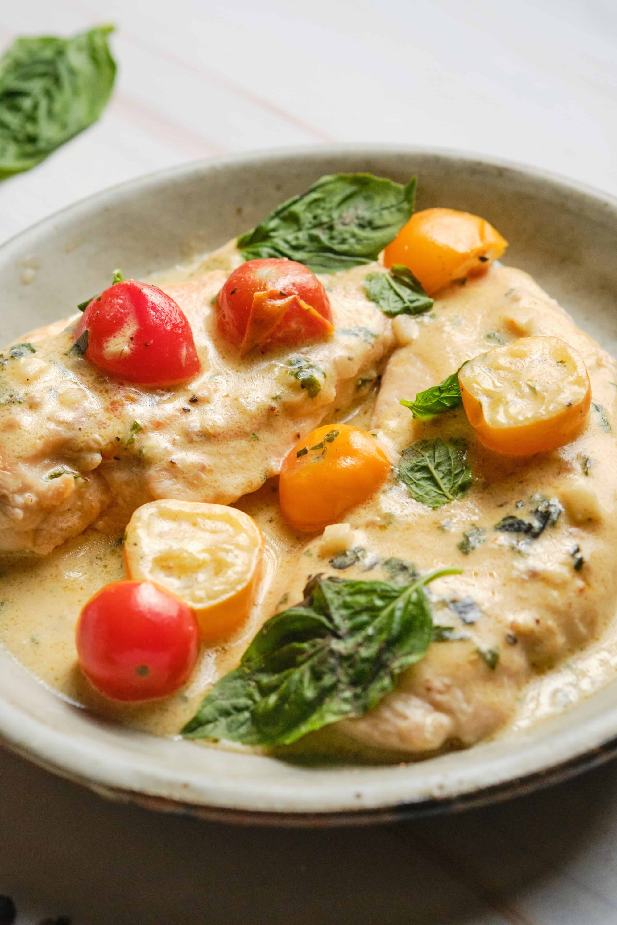 Fresh cherry tomato chicken in creamy basil sauce, served in a white bowl, featuring vibrant colorful tomatoes and fresh basil leaves.