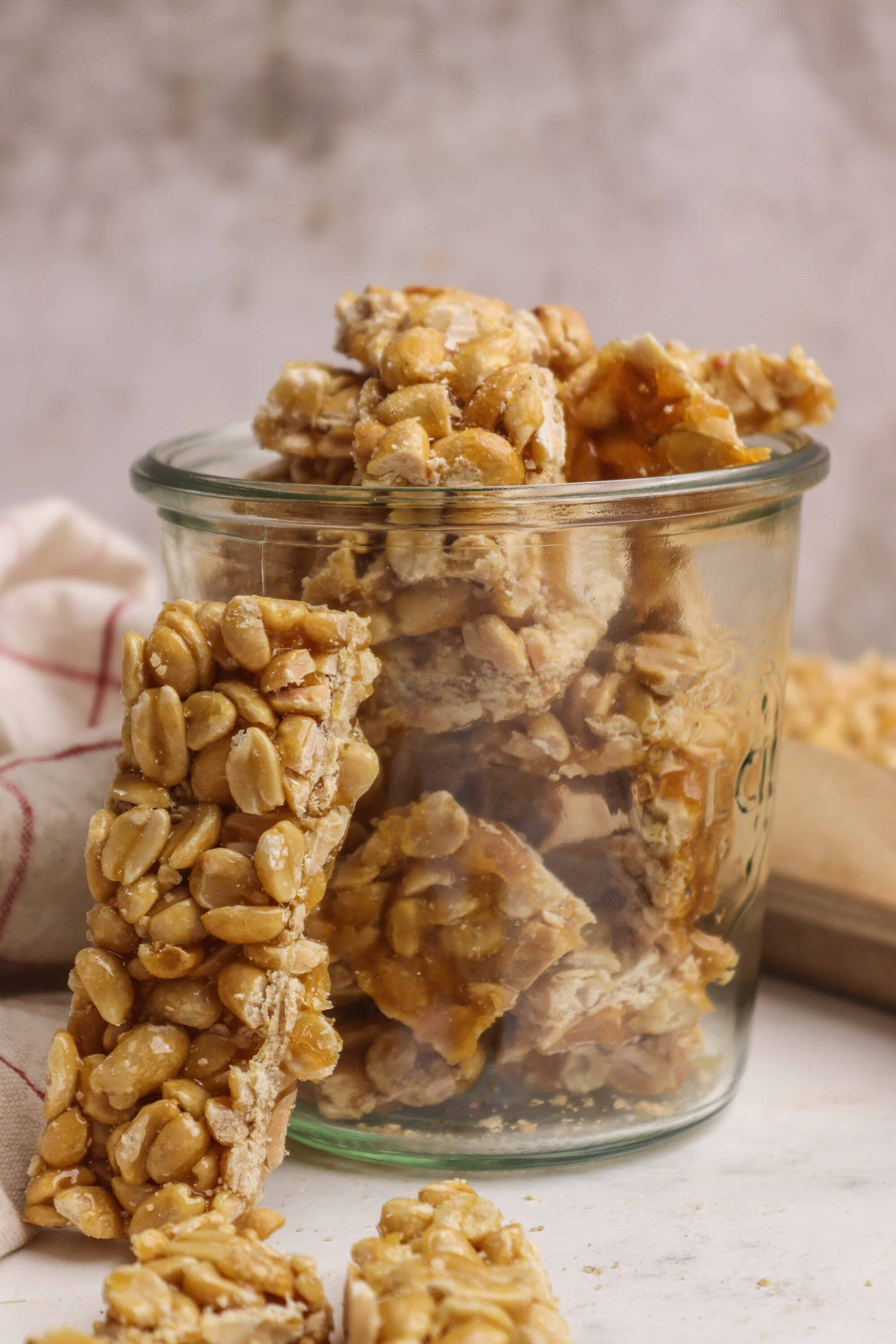 Crispy peanut brittle bars in jar with broken pieces scattered around.