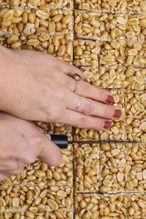 Golden peanut brittle being cut into squares with a knife.
