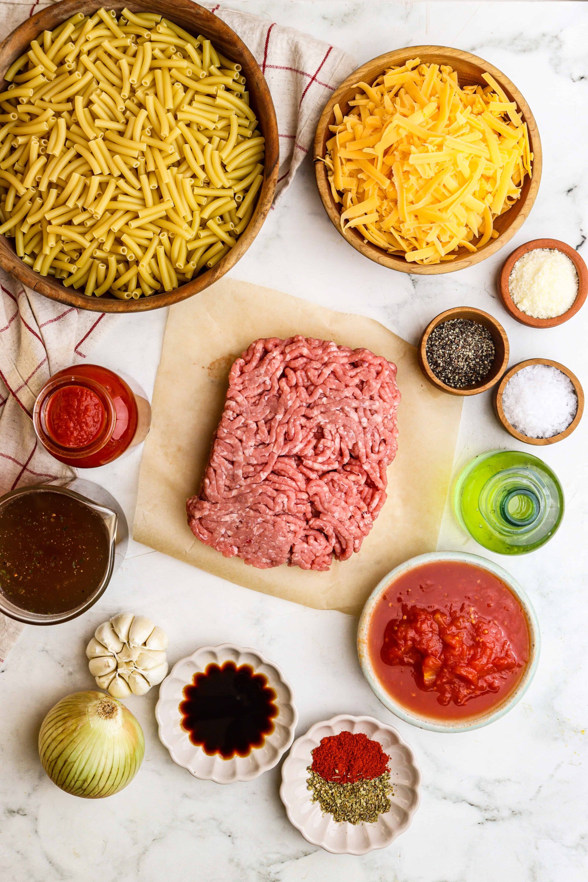 Uncooked ground beef pasta ingredients for baked ziti in a white marble countertop kitchen.