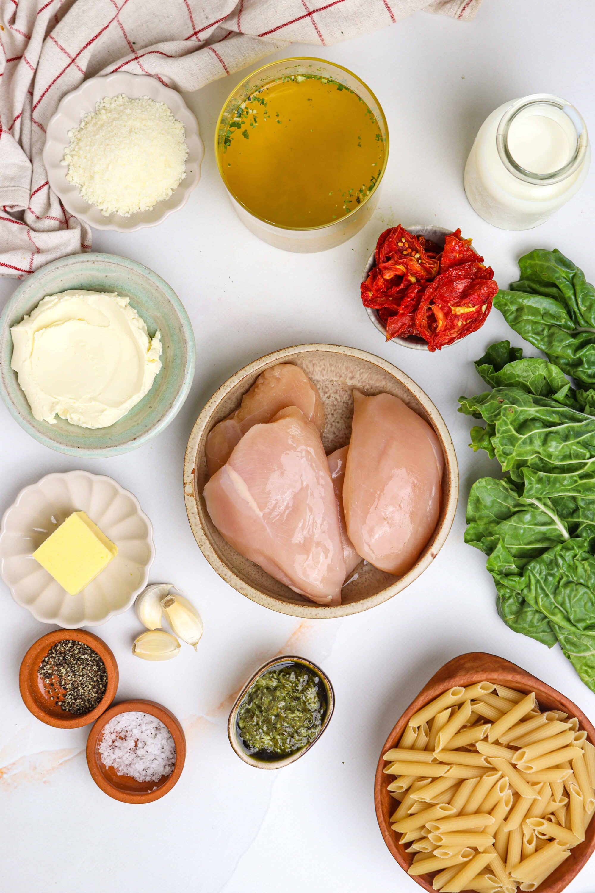 Fresh chicken pasta ingredients for homemade baked pasta dish, including chicken breasts, pasta, spinach, sun-dried tomatoes, and cheese.