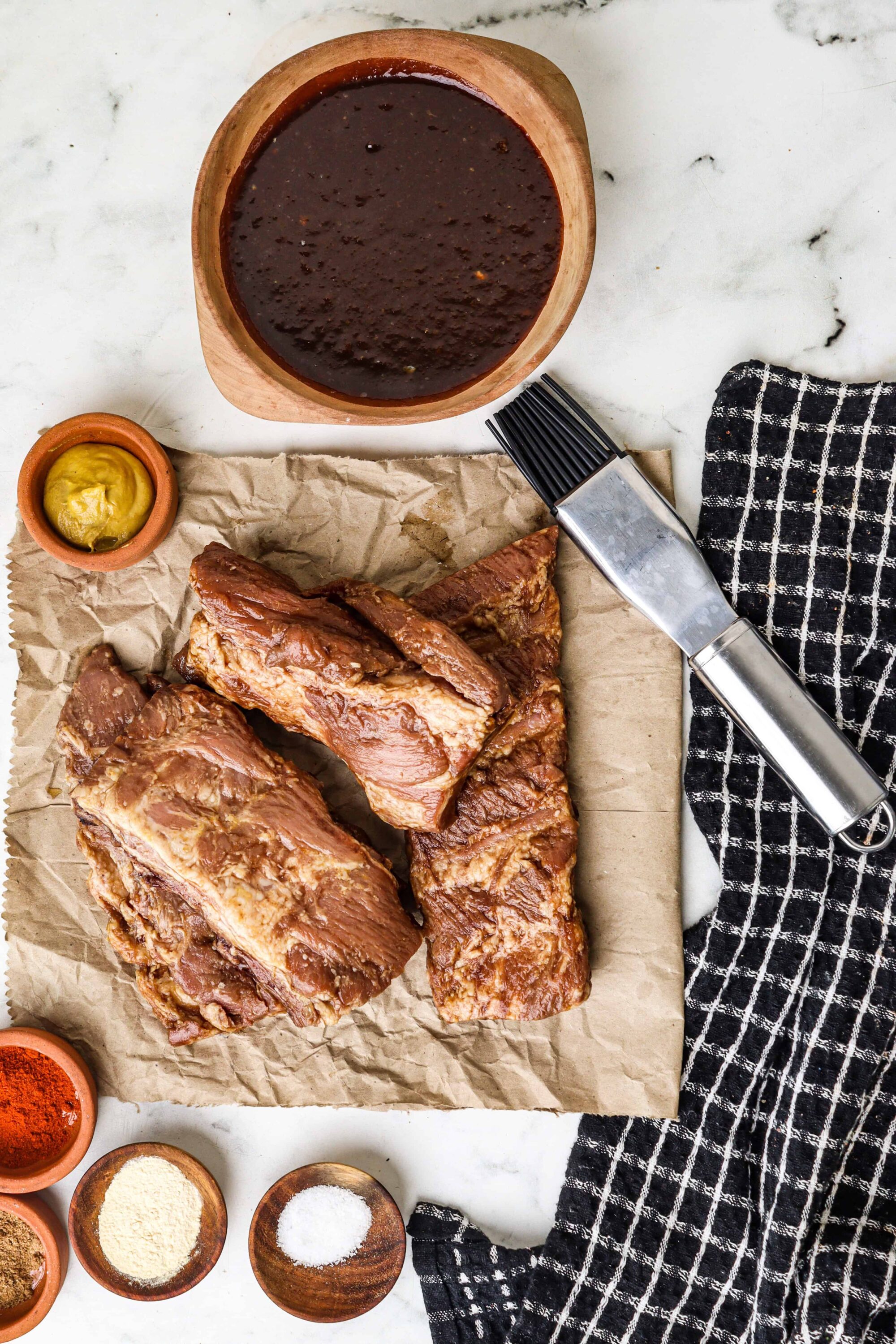 Juicy BBQ ribs with smoky sauce and condiments on parchment paper, ready to serve.