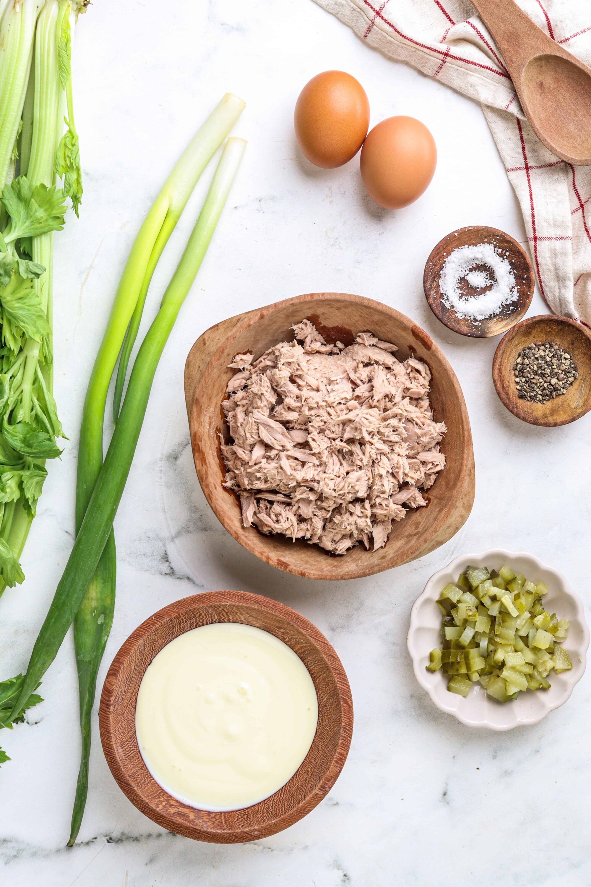Shredded chicken with celery, eggs, and seasonings on a white marble surface, preparing for a recipe.
