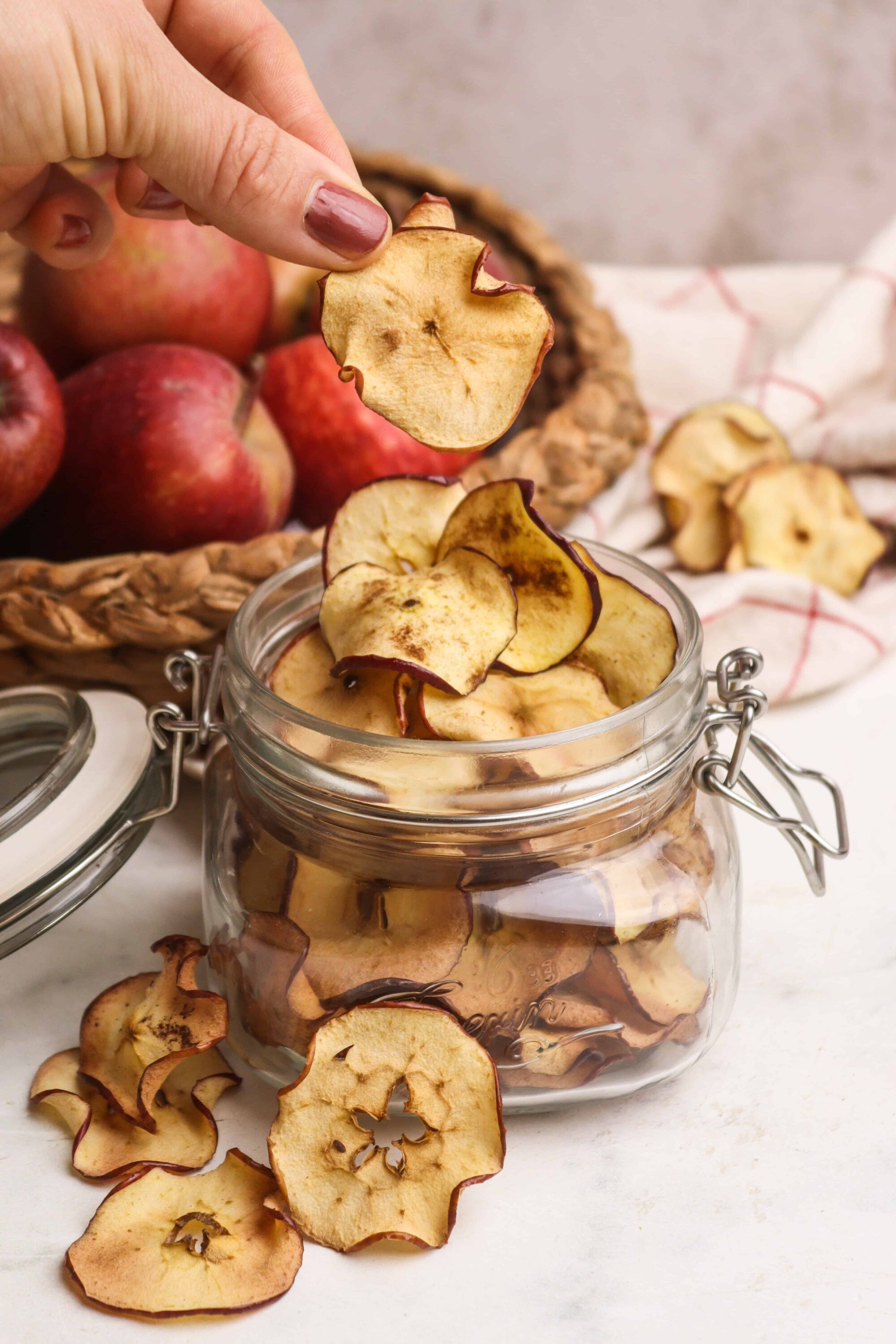Dried apple chips in glass jar with fresh apples in background.