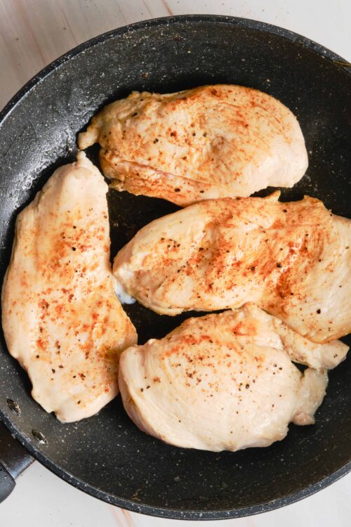 Juicy seasoned chicken breasts cooking in a black skillet.