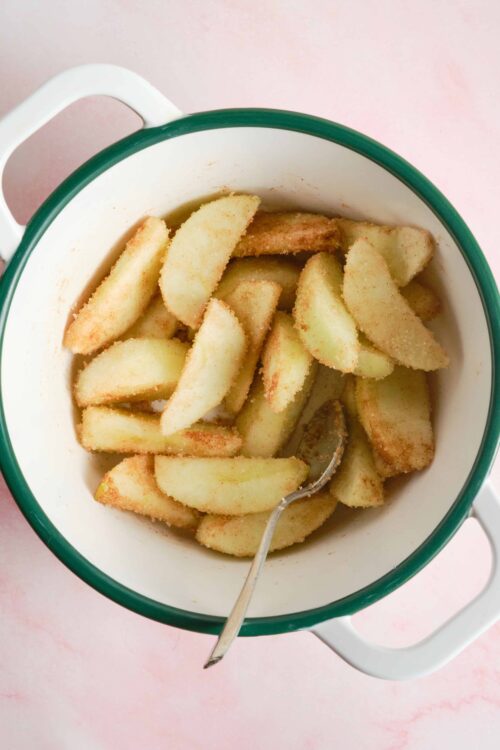 Baked apple slices in a white and green bowl on pink background.