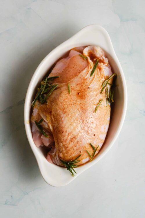 Juicy raw chicken breast seasoned with herbs in a white baking dish.