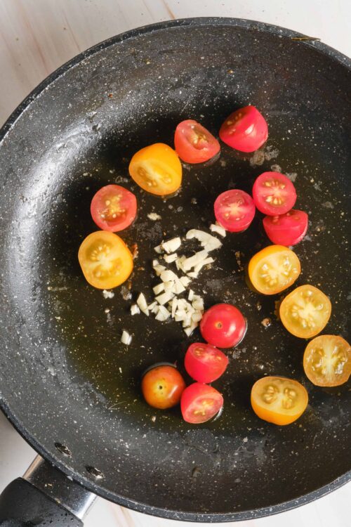 Fresh cherry tomatoes and chopped garlic sizzling in a black skillet for a delicious homemade sauté.
