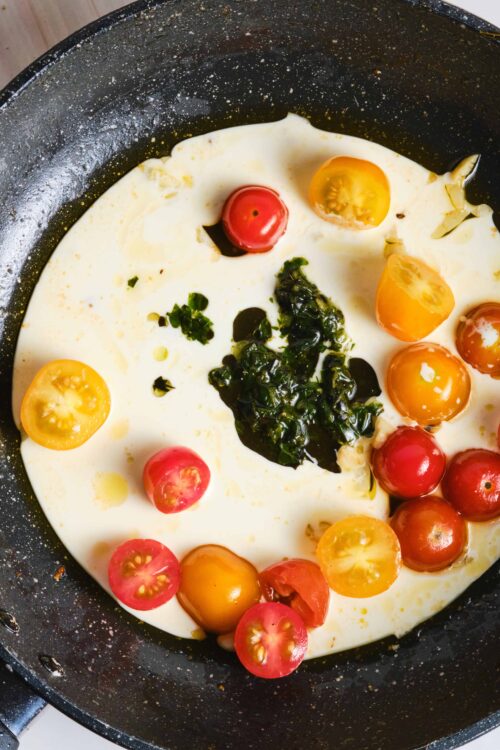Juicy cherry tomatoes cooking in a creamy scrambled eggs mixture in a black skillet.