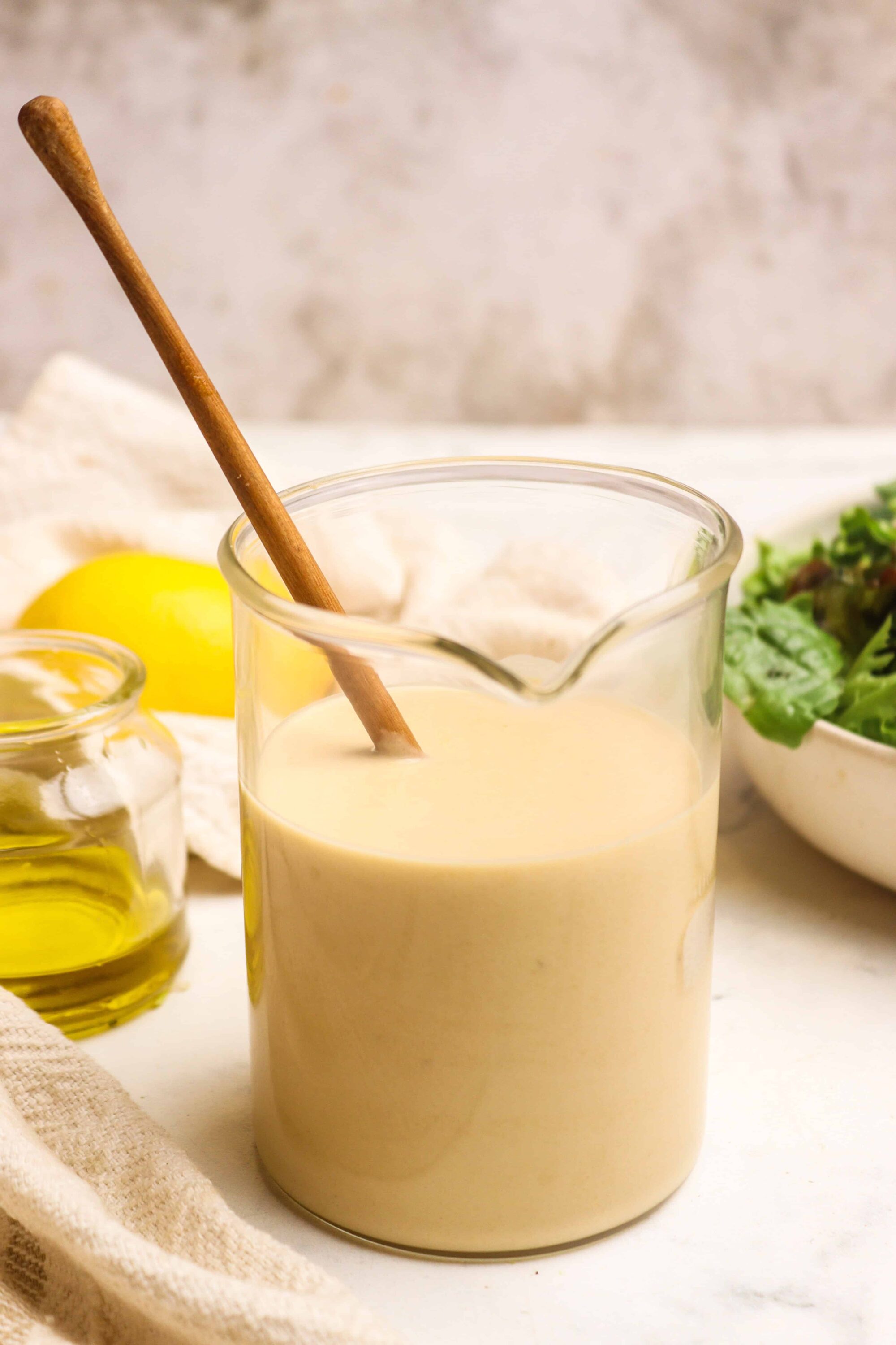 Creamy Caesar salad dressing in a glass jar with a wooden spoon, surrounded by fresh ingredients.