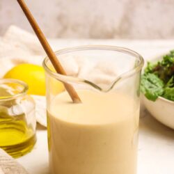 Creamy Caesar salad dressing in a glass jar with a wooden spoon, surrounded by fresh ingredients.