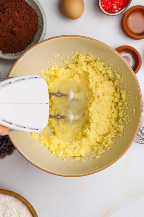 Fluffy buttercream being whipped in a mixing bowl with baking ingredients around.