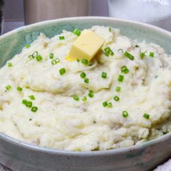 Creamy mashed potatoes with butter and chives in a rustic bowl, on a cozy kitchen counter.