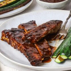 Baked Bree: BBQ ribs with zucchini and dipping sauce on a white plate.