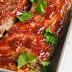 Juicy baked pork chops with tomato sauce garnished with fresh cilantro in a baking dish.