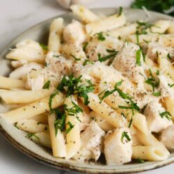 Creamy chicken and pasta Alfredo dish garnished with fresh herbs and grated cheese.